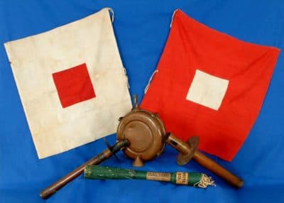 A color photograph of two museum-quality signal flags. One is red with a white square; the other is white with a red square.