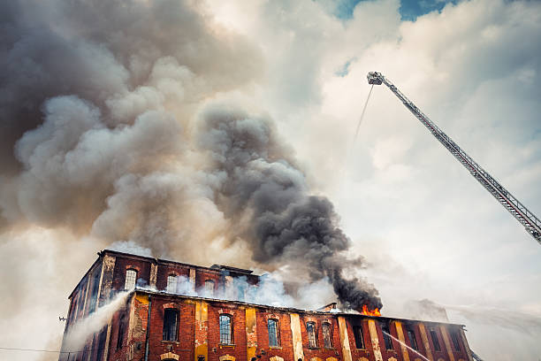 A burning brick building with great grey plumes of fire rising from the rooftop.