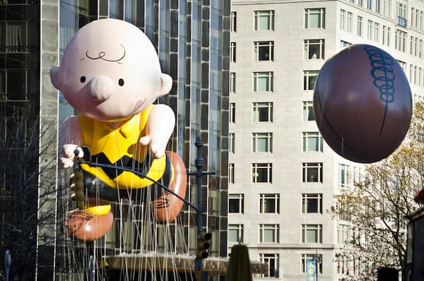 Charlie Brown balloon. He's floating down Central Park West. A separate balloon of a football follows behind him.