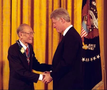 color press photograph of Clinton shaking hands with Korematsu who is wearing the medal.