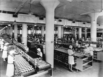 Overhead view of a candy factory. Visible are the lights and the air conditioning and many working women in white uniforms. 