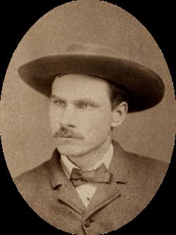Sepia-toned portrait of Frank Butler wearing a wide-brimmed hat, suit jacket, and bow tie, with a mustache and a neutral expression, looking slightly to the side. Oval frame around the image.