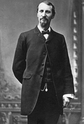 This is a formal portrait photograph of Fred Harvey in business attire. He has a Van Dyke beard and moustache. He wears a dark bow tie.