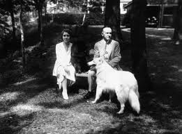 The black-and-white photo shows the couple sitting with one of their white collies.