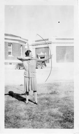 Photograph of Ina Gittings in a dress practicing archery