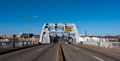 This is a color photo from istock that shows the road leading across the Edmund Pettus Bridge. The sky is blue. There are no people in this photo