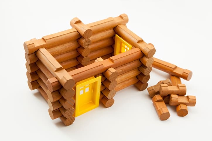 A color photograph of new Lincoln logs being used. There is a cheeful plastic yellow door that children can add.