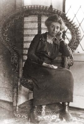 This is a black-and-white photo of architect Mary Jane Elizabeth Colter at middle age. She sits in a large rattan chair, posing for the camera.