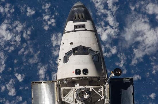 Photo of nose of the Discovery space shuttle against a blue sky with light clouds.