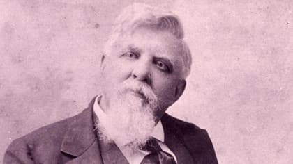 A sepia toned photo of Judge Isaac Parker.  He is dressed in a suit and has a big bushy white beard.