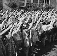 Black and white photo of children saying the Pledge of Allegiance. Initally, the right arm straight up and forward was the "salute." Today we don't use it as it is associated with the Nazis.