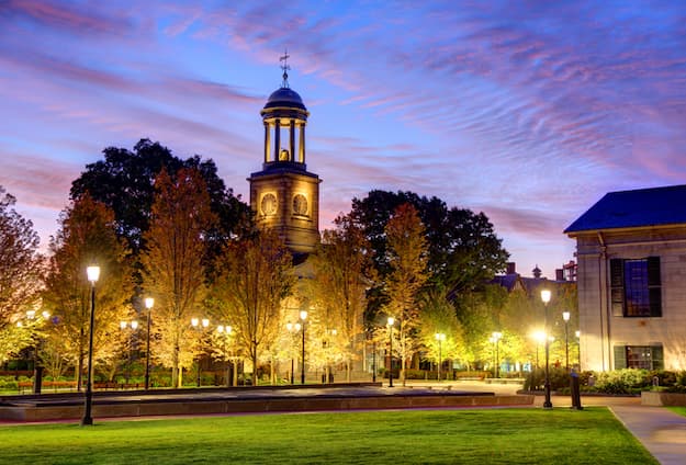 A recent color photograph of Kilroy Square in Quincy, Massachusetts. The lights around the square glimmer, and a clock tower can be seen in the background.