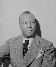 In this black-and-white photograph of Randolph, who headed the Brotherhood of Sleeping Car Porters, he is dressed in a suit. His hair is cropped short, and he is looking to the right of the photographer