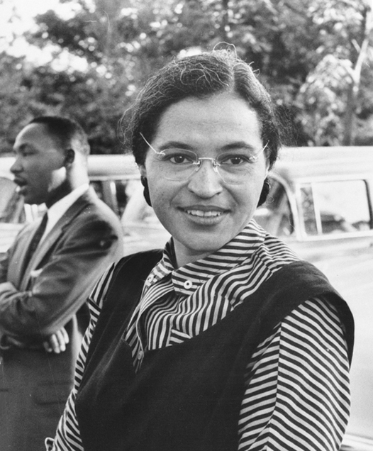 a black-and-white photograth of Rosa Parks with Martin Luther King standing behind her in conversation with someone.  public domain