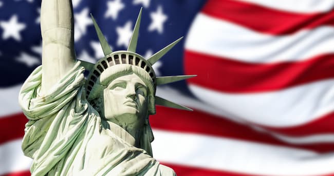 Color photo of head and shoulders of the Statue of Liberty with the American flag behind. istockphoto.com