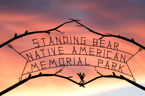 A photograph of the red morning sky with the Standing Bear Memorial Park sign in the foreground. Ponca City. istockphotos