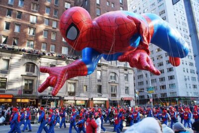 A beautiful color photo of the Spiderman balloon floating down Broadway. You can see the balloon handlers who are also dressed in red and blue as is Spiderman