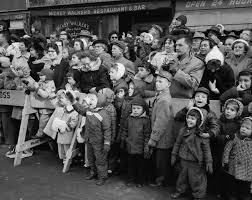 A photograph of a big crowd watching the parade. The photo is in black-and-white and is likely from the late 1940s or early 1950s.