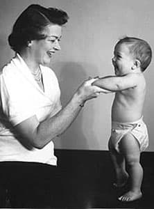 Press photograph of Donovan with standing baby modeling her invention, the diaper cover.