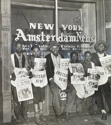 Six children stand outside the Black-owned New York Amsterdam News office wearing newspaper bags and holding copies of the paper.