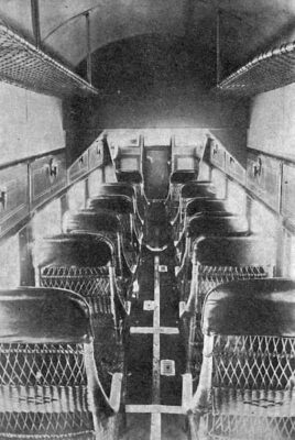This black-and-white photograph shows six rows of seats inside the plane. There is only one seat on each side of the aisle, and the chairs are made of a basket-weave material.