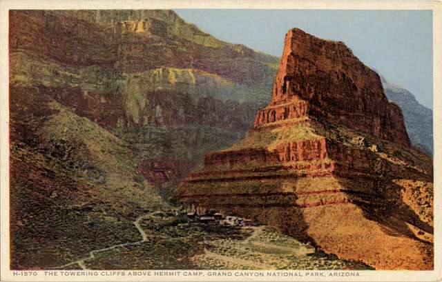 This is a postcard of the towering cliffs above a Fred Harvey location, Hermit Camp. There is a mountain road and red towering cliffs. A beautiful photo