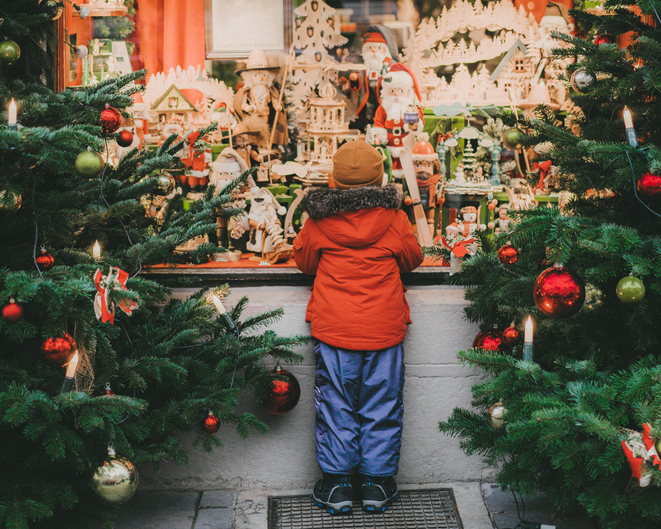 Color photo of a child peering in a window filled with toys and fun things for the holidays.