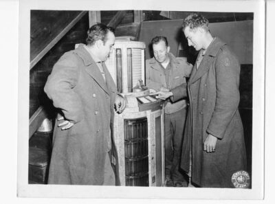 A black-and-white photo of members of the military listening to a jukebox.