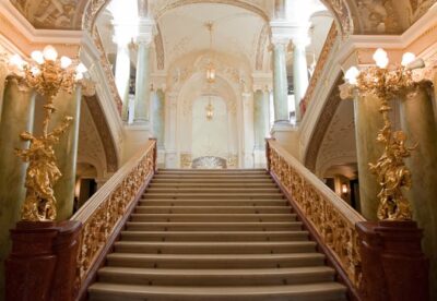 This is a grand staircase of what might be amovie palace. Gold encrusted statues and handrail, and a wide and beautiful staircase. istockphoto.com