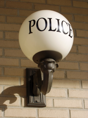 A round white lamp with the word POLICE mounted on a brick wall, commonly seen outside police stations, serves as a symbol of security in accordance with traditions established around the Security 1908 Convention.