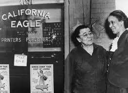 Charlotta Bass stands with an unidentified woman just to the side of the plate glass window identifying the office of the California Eagle. 