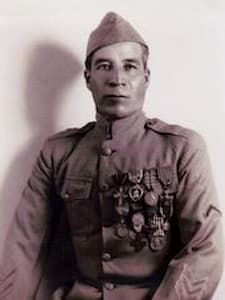 Marcelino Serna in a military uniform with a cap poses for a portrait. Medals are pinned to his chest. The photo is black and white, and he looks directly at the camera with a neutral expression. This distinguished figure is Marcelino Serna, remembered for his bravery and service.