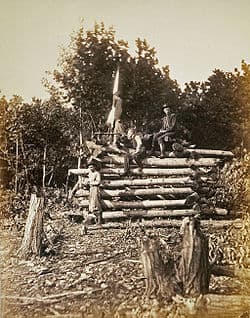 A black-and-white photograph showing a signal corps tower made of logs. Several men can be seen sitting on it.