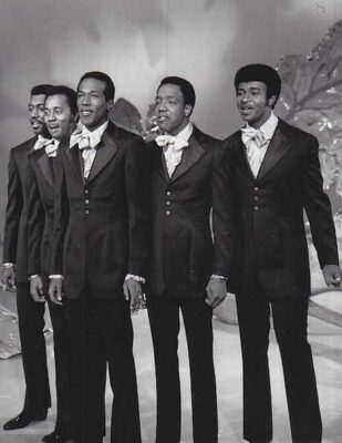 This black-and-white photo shows five of the Temptations, all dressed in dark suits and ready to perform.