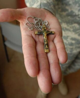 A hand holds for display a silver and perhaps gold crucifix attached to a chain that Kilmer may have worn around his neck.