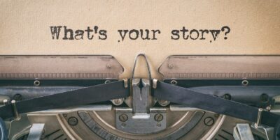 A photo of typed copy on a ribbon typewriter. The type says What's your story?
