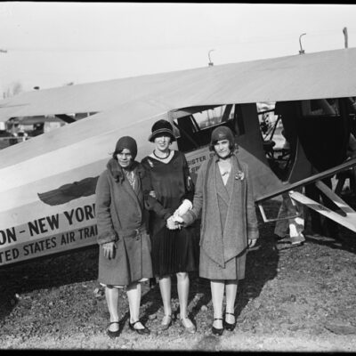 women standing by early airplane 1928