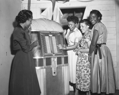This black-and-white photo probably dates to the 1940s and shows four Black women enjoying themselves by the jukebox.
